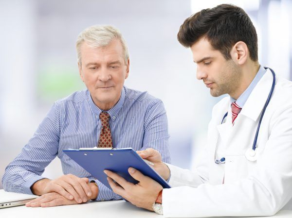 Portrait of young male doctor sitting at desk with elderly patient and consulting at hospital.