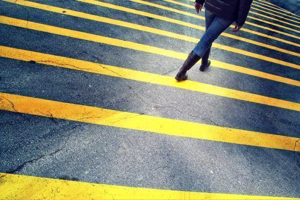 Lonely woman walk on asphalt street with marked yellow lines.
