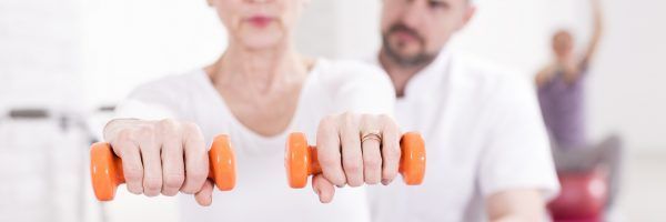 Close up of a mature woman exercising with dumbbells and her instructor, panorama