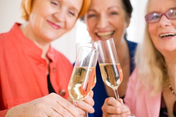Three Smiling Mom Friends Tossing Glasses of Champagne Celebrating their Friendship. Captured in Macro.
