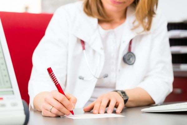 Young gynaecologist writing medical prescription in surgery at desk
