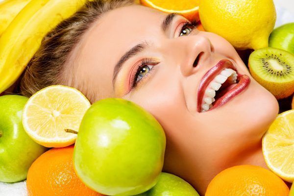 Close-up portrait of a beautiful smiling woman among fresh fruts. Healthy eating, juice. Make-up, cosmetics. Healthy teeth.