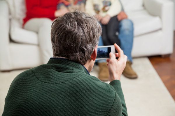 Rear view of father photographing family through smartphone at home