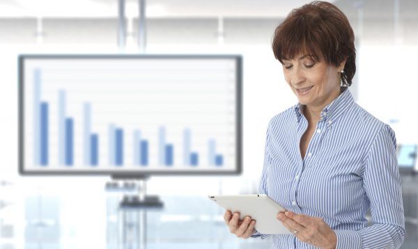 Senior casual caucasian female business executive looking at results on tablet at office with chart in background. Standing, copyspace.