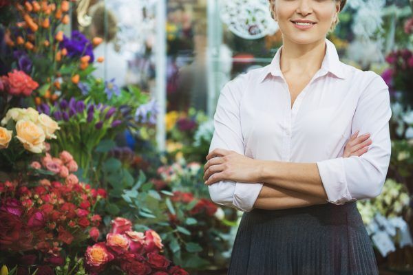 Friendly saleswoman is standing near abundance of roses and smiling