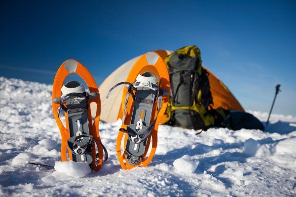 Snowshoes left in front of orange tent in winter forest
