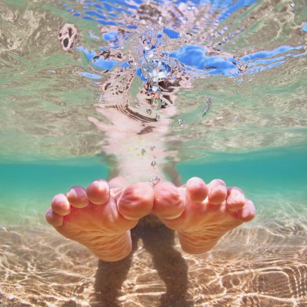 Funny underwater photo of happy bare foot baby girl sitting with fun in sea pool. Healthy lifestyle, people water sport outdoor activities, swimming lessons on summer beach family holidays with child.