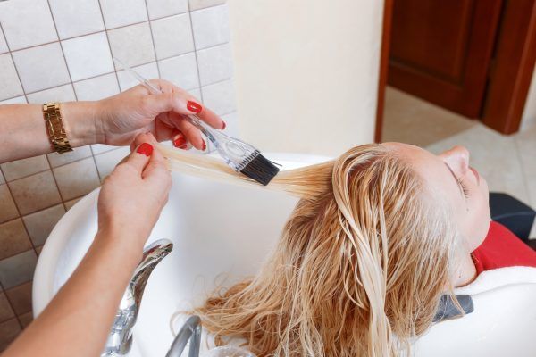 The hairdresser applies the paint on the client's white hair before painting over the washbasin in the beauty salon.