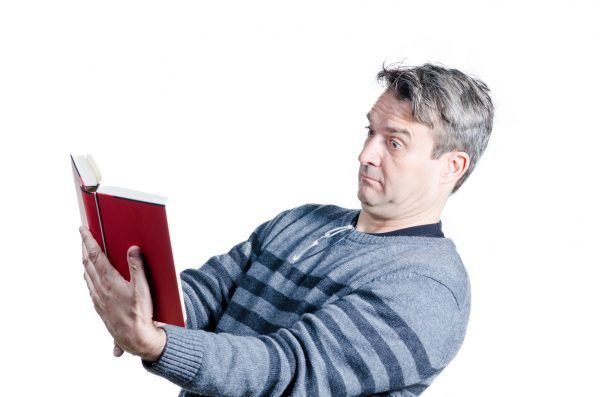 Guy finding holding a book at quite a distance to be able to read