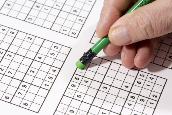 An elderly man is doing sudoku. He has filled some numbers already and now he is rubbing it off. This is a good workout for brains on older people.