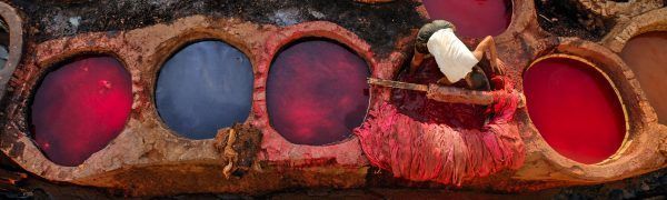 Worker dying leather in colorful red tanks in a traditional tannery in Fes, Morocco