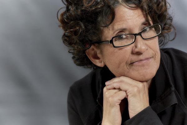 Middle aged woman with curly brown hair wearing black reading glasses and smiling