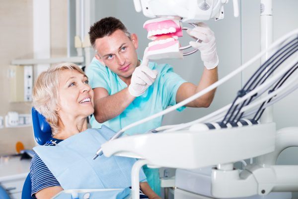 Professional dentist explaining to his female patient correct tooth brushing on dental model. Focus on woman