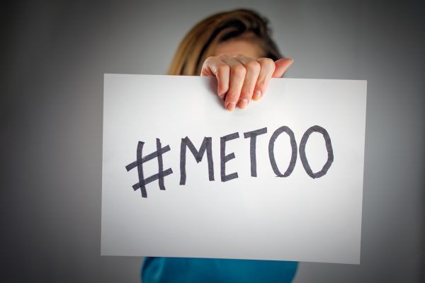 a young woman holds a banner with the inscription "#metoo" in front of her. Blue sweater, long hair. Me Too movement. selective focus , blurred neutral background, vignetting